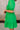 Close-up side view of female model wearing the Lea Green Puff Sleeve Mini Dress that has kelly green fabric, a smocked upper with high neck, short puff sleeves, and mini length. Model is holding coffee and has purse on shoulder.
