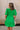 Back view of female model wearing the Lea Green Puff Sleeve Mini Dress that has kelly green fabric, a smocked upper with high neck, short puff sleeves, and mini length. Model is holding coffee and has purse on shoulder.