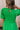 Upper body back view of female model wearing the Lea Green Puff Sleeve Mini Dress that has kelly green fabric, a smocked upper with high neck, short puff sleeves, and mini length. Model is holding coffee and has purse on shoulder.