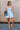 Full body front view of female model wearing the Taylor Light Wash Denim Romper that has light wash denim fabric, straps with frayed hems, elastic waist, neckline pleating, and side pockets.