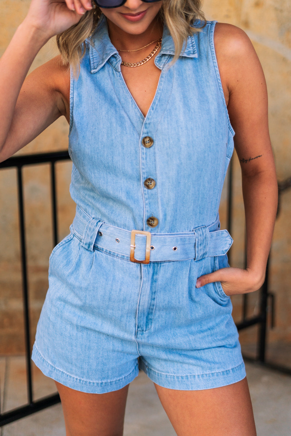 Close front view of female model wearing the Georgia Belted Denim Romper in light wash, that has a button up front, collar, and belted waist.