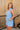 Side view of female model wearing the Georgia Belted Denim Romper in light wash, that has a button up front, collar, and belted waist.