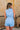 Back view of female model wearing the Georgia Belted Denim Romper in light wash, that has a button up front, collar, and belted waist.