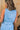 Upper body back view of female model wearing the Georgia Belted Denim Romper in light wash, that has a button up front, collar, and belted waist.