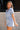 Side view of female model wearing the Mavis Denim Short Sleeve Zip-Up Romper which features Denim Fabric, Two Front Pockets, Front Zipper Closure, Adjustable Monochrome Belt with Loops, Collared Neckline and Short Sleeves