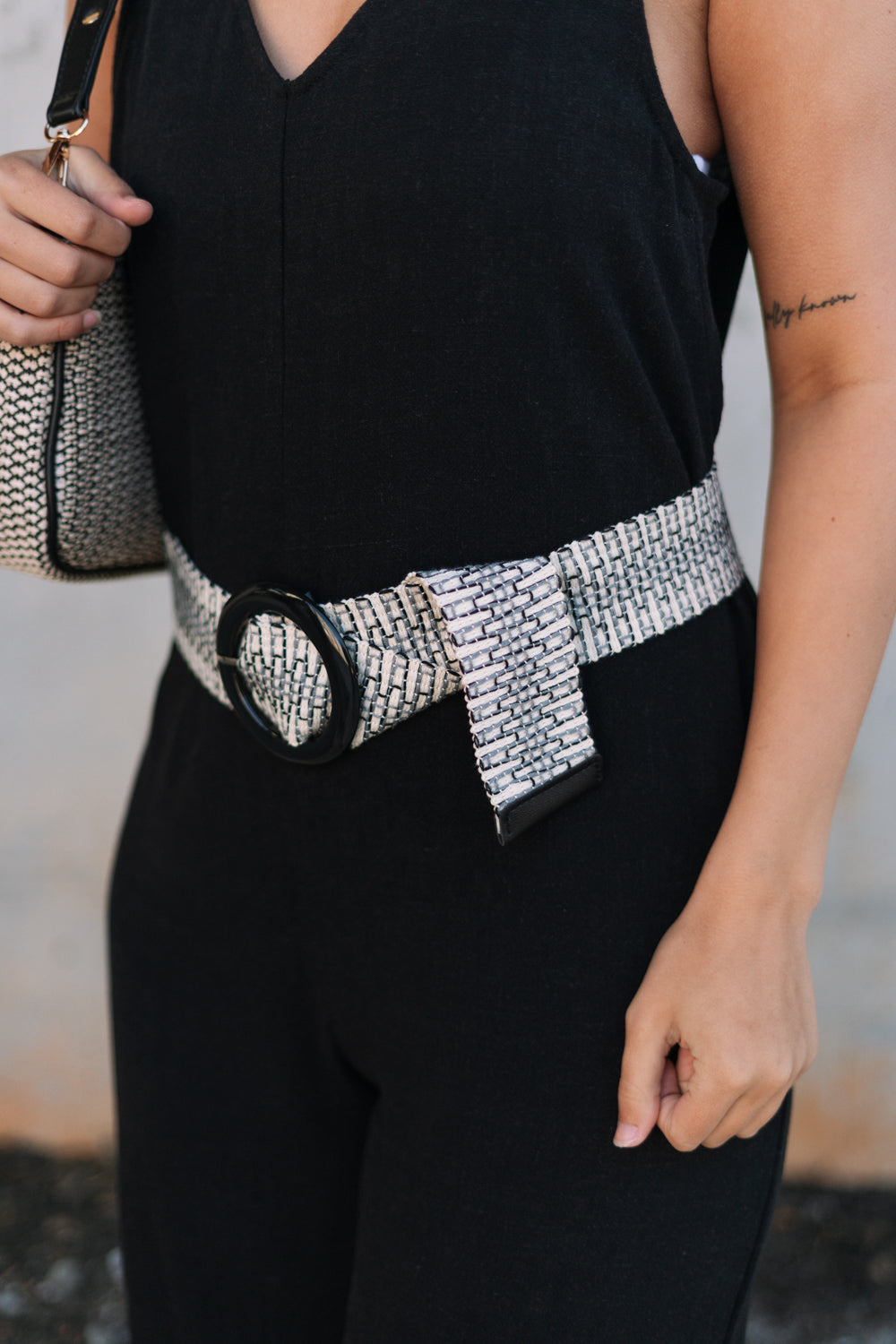 SIde view of female model wearing the Taryn Black & Natural Woven Belt which features Natural Woven Fabric, Black and Grey Wave Thread Design and Black Acrylic Adjustable Buckle