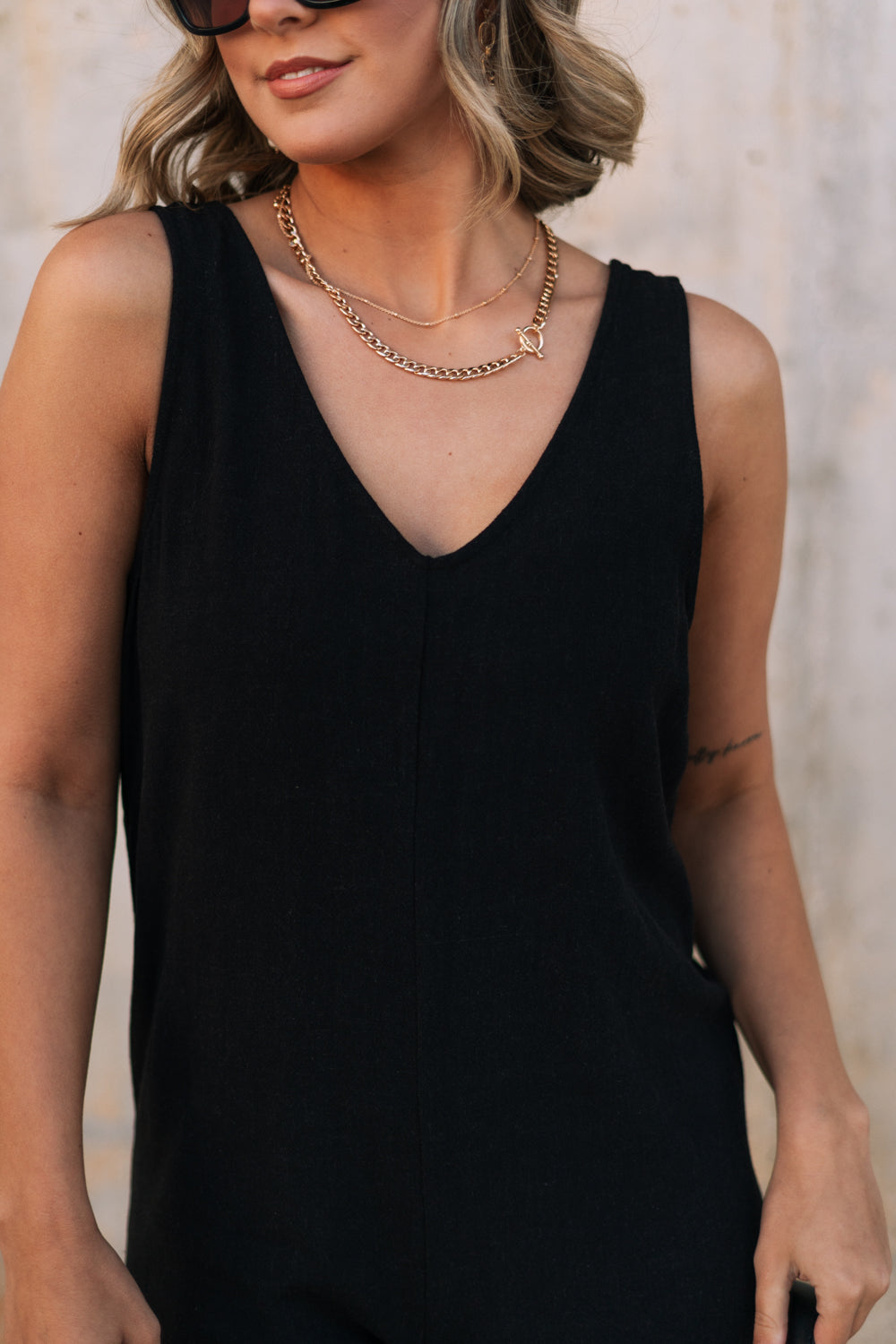 Upper body front view of female model wearing the Kinsley Black Sleeveless Jumpsuit that has black lightweight fabric, thick straps, wide legs, and a v-neck. 