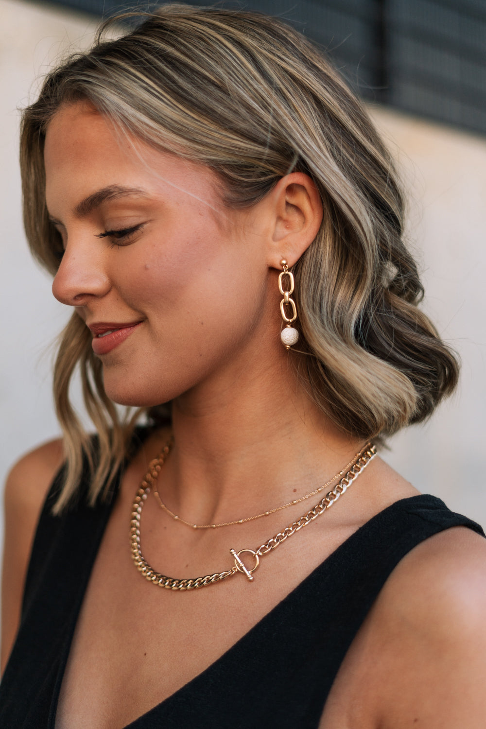 Side view of female model wearing the Rhodes Gold & Cream Chain Dangle Earring which features gold chain link dangle earrings with cream textured beads