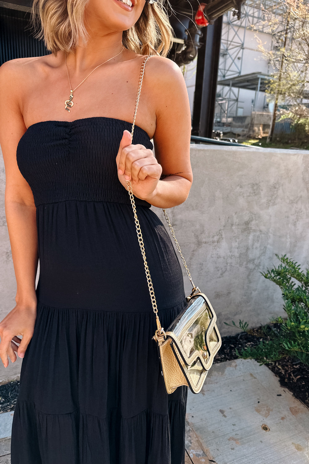 Side view of female model wearing the Miley Clear Purse in Gold which features clear with leather details, gold snap closure, and an adjustable gold chain strap with gold details.
