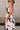 Close-up upper body side view of female model wearing the Elina Printed Button Front Midi Dress that has ivory, black, and orange geometric printing, a tie belt, a button up front, a collared sleeveless neckline, and midi length.