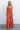 Full body front view of female model wearing the Jules Orange Printed Wide Leg Jumpsuit that has orange printed fabric, thin straps, and wide legs.