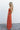 Full body side view of female model wearing the Jules Orange Printed Wide Leg Jumpsuit that has orange printed fabric, thin straps, and wide legs.