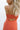 Upper body back view of female model wearing the Jules Orange Printed Wide Leg Jumpsuit that has orange printed fabric, thin straps, and wide legs.