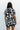 Upper body back view of female model wearing the Valerie Black & White Short Sleeve Romper that has a black and white abstract print, short sleeves, a collar, button up front, and elastic waist with tie.