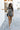 Full body front view of female model wearing the Valerie Black & White Short Sleeve Romper that has a black and white abstract print, short sleeves, a collar, button up front, and elastic waist with tie.
