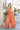 Full body front view of female model wearing the Jules Orange Printed Wide Leg Jumpsuit that has orange printed fabric, thin straps, and wide legs.