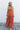 Full body front view of female model wearing the Jules Orange Printed Wide Leg Jumpsuit that has orange printed fabric, thin straps, and wide legs.