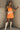 full body view of female model wearing the Amaya Strapless Flare Mini Dress in Orange which features Lightweight Fabric, Side Zipper Closure, Belt Loops, Two Front Pockets, Strapless and Shorts Lining.  Worn with white belt