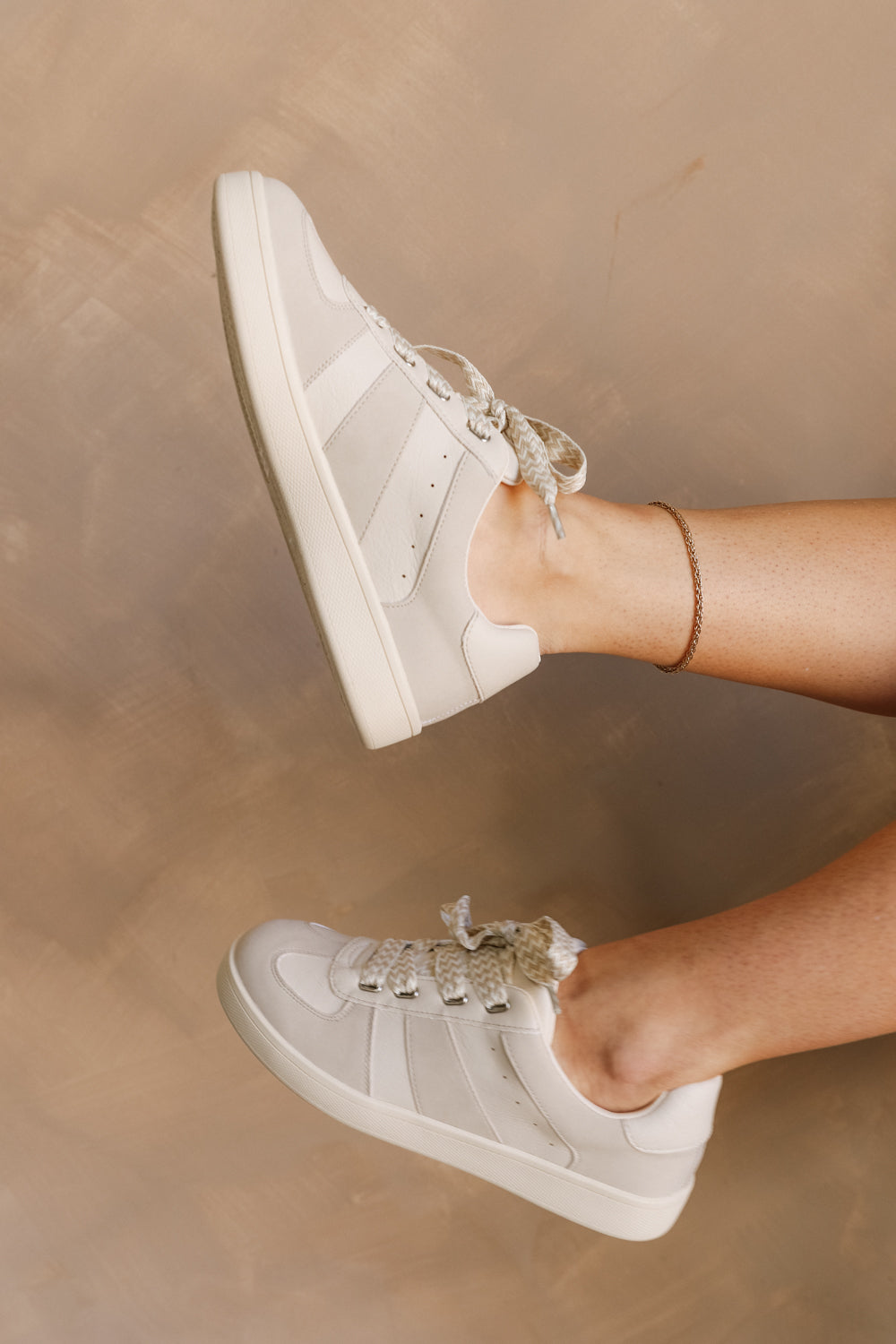 Side view of female model wearing the Vibe Sneaker in Off White which features Off White and White Upper Leather, Round Toe,  Zig-Zag Print Design Lace Up Details and Pull Tab 
