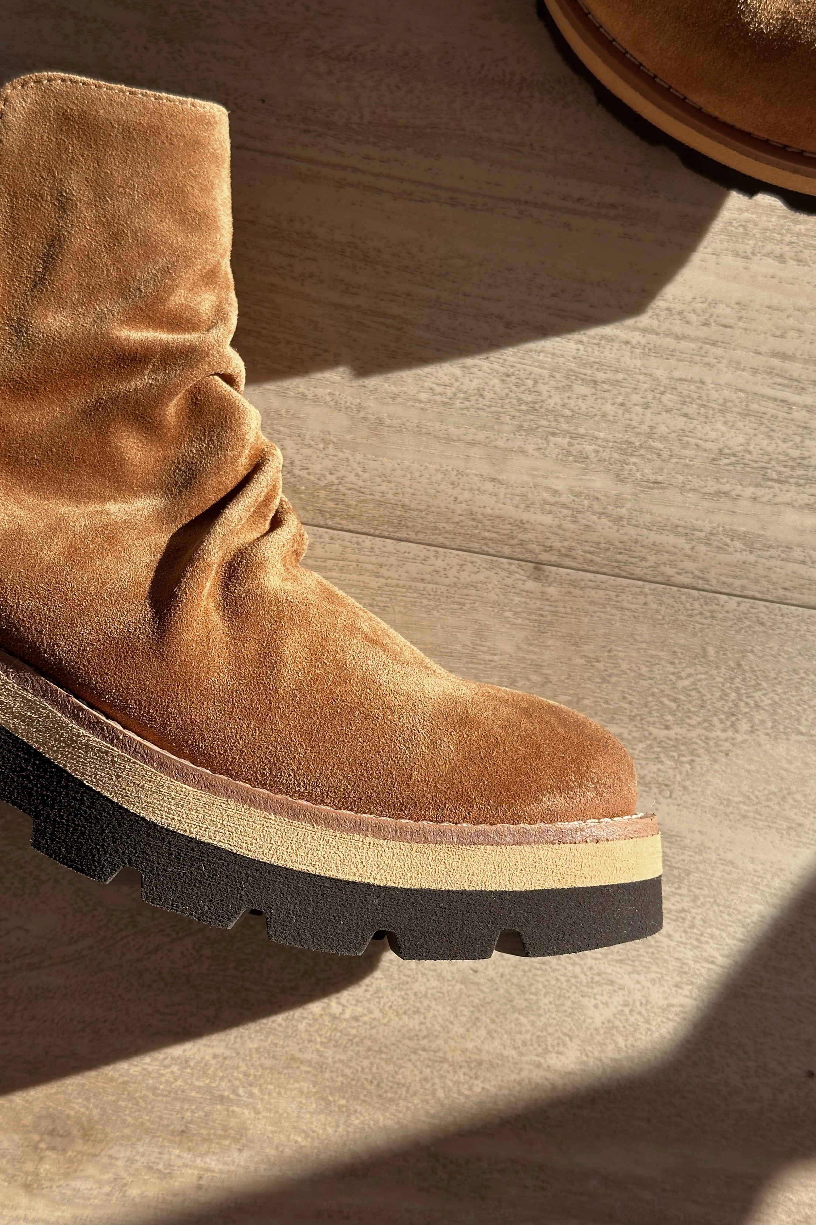 Close up view of the Pecola Boot in Brandy which features light brown water-resistant suede fabric, slouch details, black lug sole, inside zipper, arch support and 2 inch heel height
