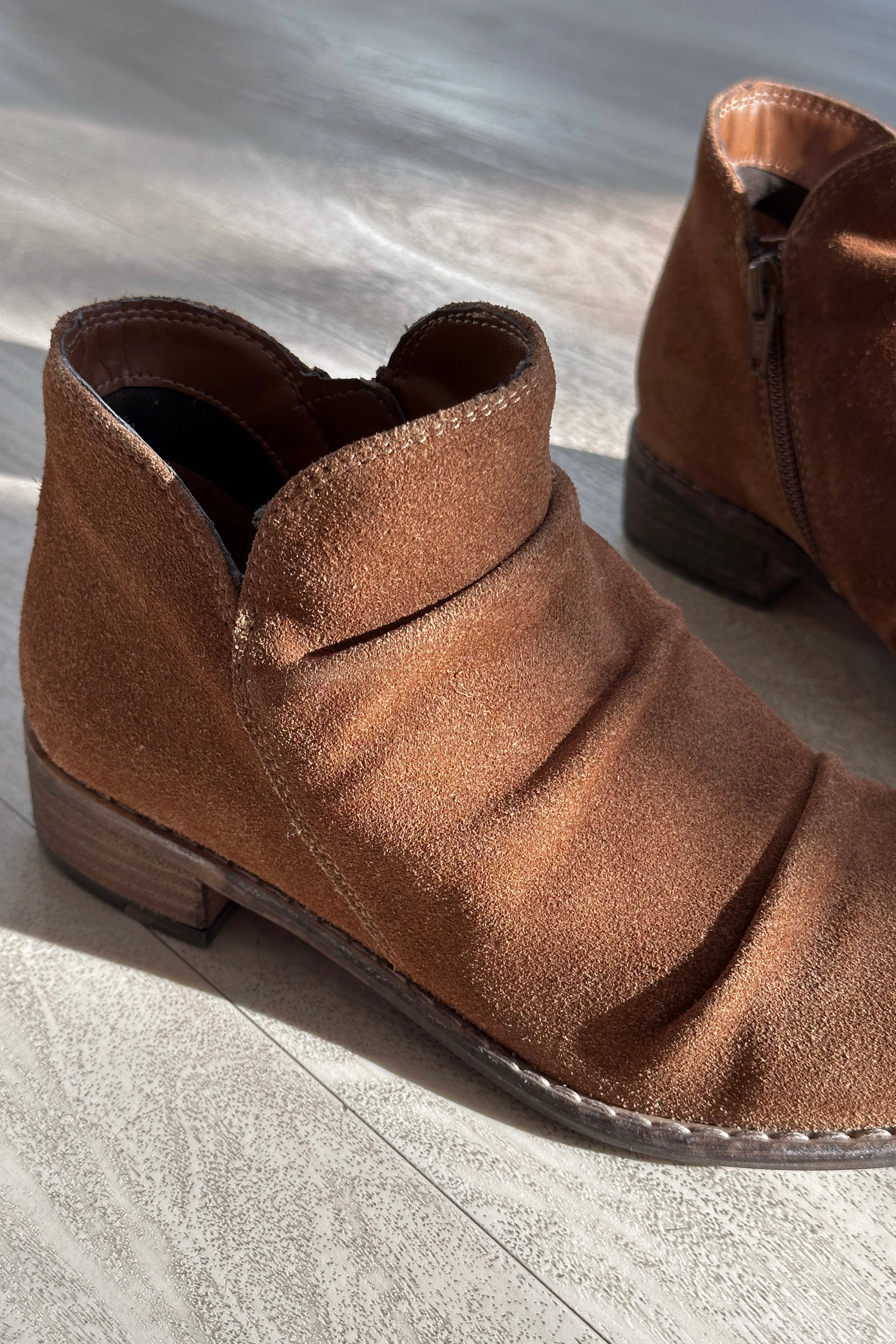 Close up view of the Rose Mera Bootie in Tan Suede which features light brown suede fabric, slouched details, inside zipper closure, round toe, lightly cushioned footbed and 1.25" stack heel