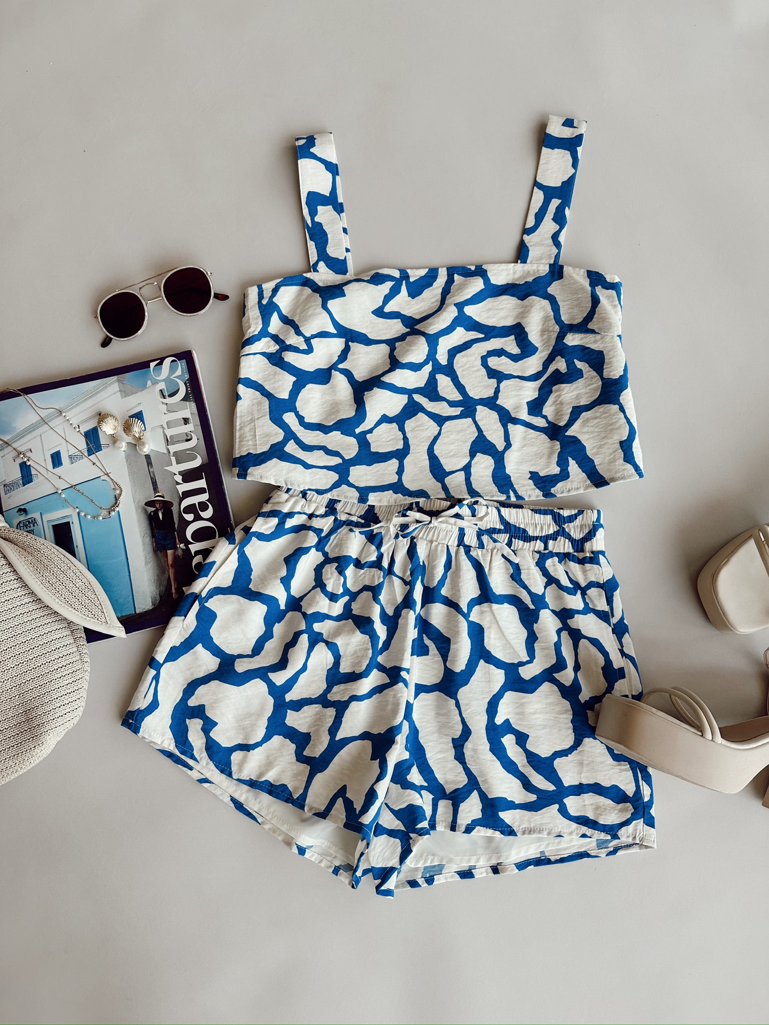 image of patterned blue and white tank & shorts laid out as a flat lay, clickable white button on image reads "shop sets"