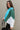 Side view of model wearing the Ashley Blue Multi Color Block Sweatshirt which features blue, green and white knit fabric, a color block pattern, textured details, a collared neckline with a v-cutout, and long sleeves with elastic cuffs.