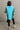 Full body back view of model wearing the Ashley Blue Multi Color Block Sweatshirt which features blue, green and white knit fabric, a color block pattern, textured details, a collared neckline with a v-cutout, and long sleeves with elastic cuffs.