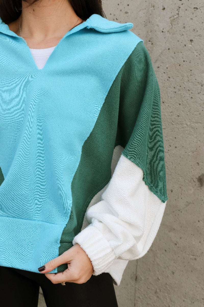 Close up view of model wearing the Ashley Blue Multi Color Block Sweatshirt which features blue, green and white knit fabric, a color block pattern, textured details, a collared neckline with a v-cutout, and long sleeves with elastic cuffs.