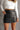 Close front view of model wearing the Bexley Black Faux-Leather Mini Skirt that has black faux leather, white stitch details, a front zipper, two front pockets, and mini length.