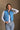 Front view of model wearing the Sutton Blue Cropped Puffer Vest that has blue puffer fabric, a  3 tiered design, medium blue lining, a cropped waist,pockets, a front zipper, a drawstring, a high neck and a sleeveless design.