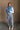 Full body front view of model wearing the Sutton Blue Cropped Puffer Vest that has blue puffer fabric, a  3 tiered design, medium blue lining, a cropped waist,pockets, a front zipper, a drawstring, a high neck and a sleeveless design.