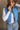 Close front view of model wearing the Sutton Blue Cropped Puffer Vest that has blue puffer fabric, a  3 tiered design, medium blue lining, a cropped waist,pockets, a front zipper, a drawstring, a high neck and a sleeveless design.