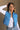 Front view of model wearing the Sutton Blue Cropped Puffer Vest that has blue puffer fabric, a  3 tiered design, medium blue lining, a cropped waist,pockets, a front zipper, a drawstring, a high neck and a sleeveless design.