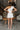 Full body back view of model wearing the All My Love Ruffle Romper which features white fabric, pockets on each side, a tie around the waist, one shoulder ruffle strap, and a monochromatic side zipper with a hook closure.