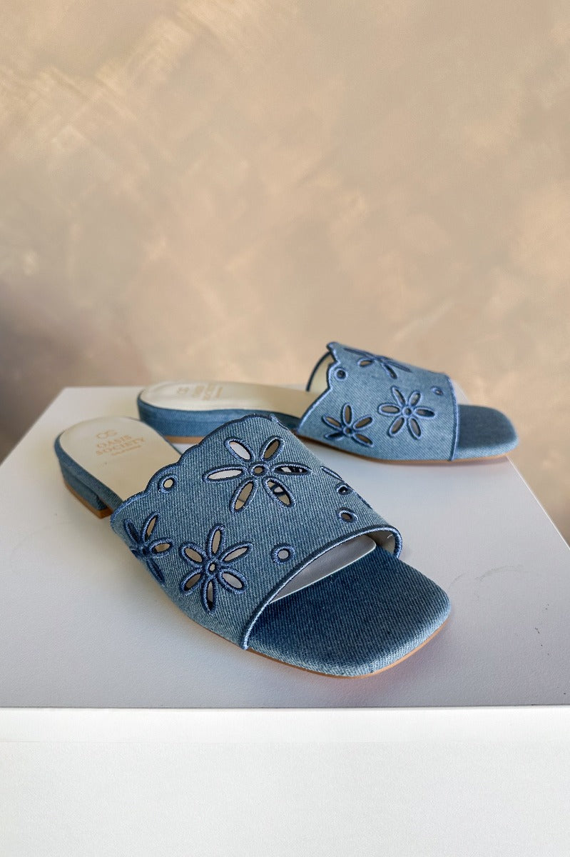 Front right angle view of the Manila Denim Eyelet Flower Heel Sandal which features blue denim fabric with eyelet flower details, square toes, backless slide entry, and 1" heels.