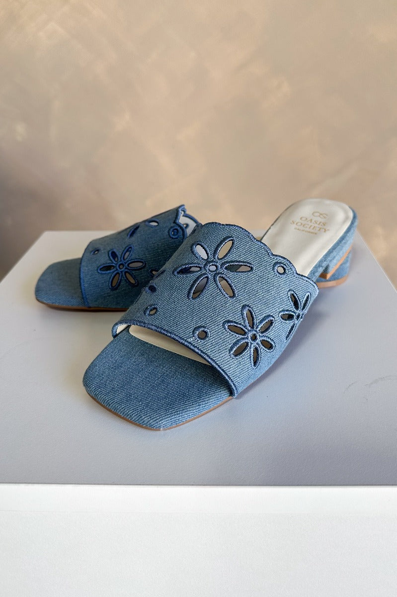 Close up view of the Manila Denim Eyelet Flower Heel Sandal which features blue denim fabric with eyelet flower details, square toes, backless slide entry, and 1" heels.
