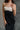 Upper front view of model wearing the Kaliyah Black & Cream Satin Midi Dress that has black, taupe and cream satin fabric, midi length, slits, a colorblock detail, a scoop neck, tie straps, and an open back.