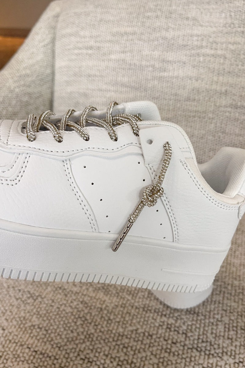 Close side view of the Eden Sneakers that have white faux-leather uppers, platform soles, and rhinestone laces.