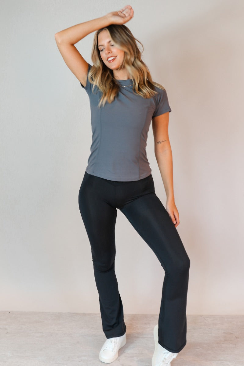 Full body view of model wearing the Robin Grey Athletic Short Sleeve Top which features grey athleisure fabric, monochrome stitch details, a scooped neckline, and short sleeves.