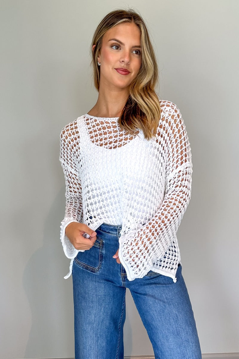 Front view of model wearing the Sahara Ivory Crochet Knit Long Sleeve Sweater which features ivory open knit fabric, a high-low hem, slits on each side, a round neckline and long flare sleeves.