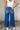 Back view of model wearing the Ceros: Florence Medium Wash Wide Leg Jeans which features medium blue denim fabric, a front zipper with a button closure, belt loops, a super high-rise waist, two front pockets, two back pockets, and wide cropped legs with d