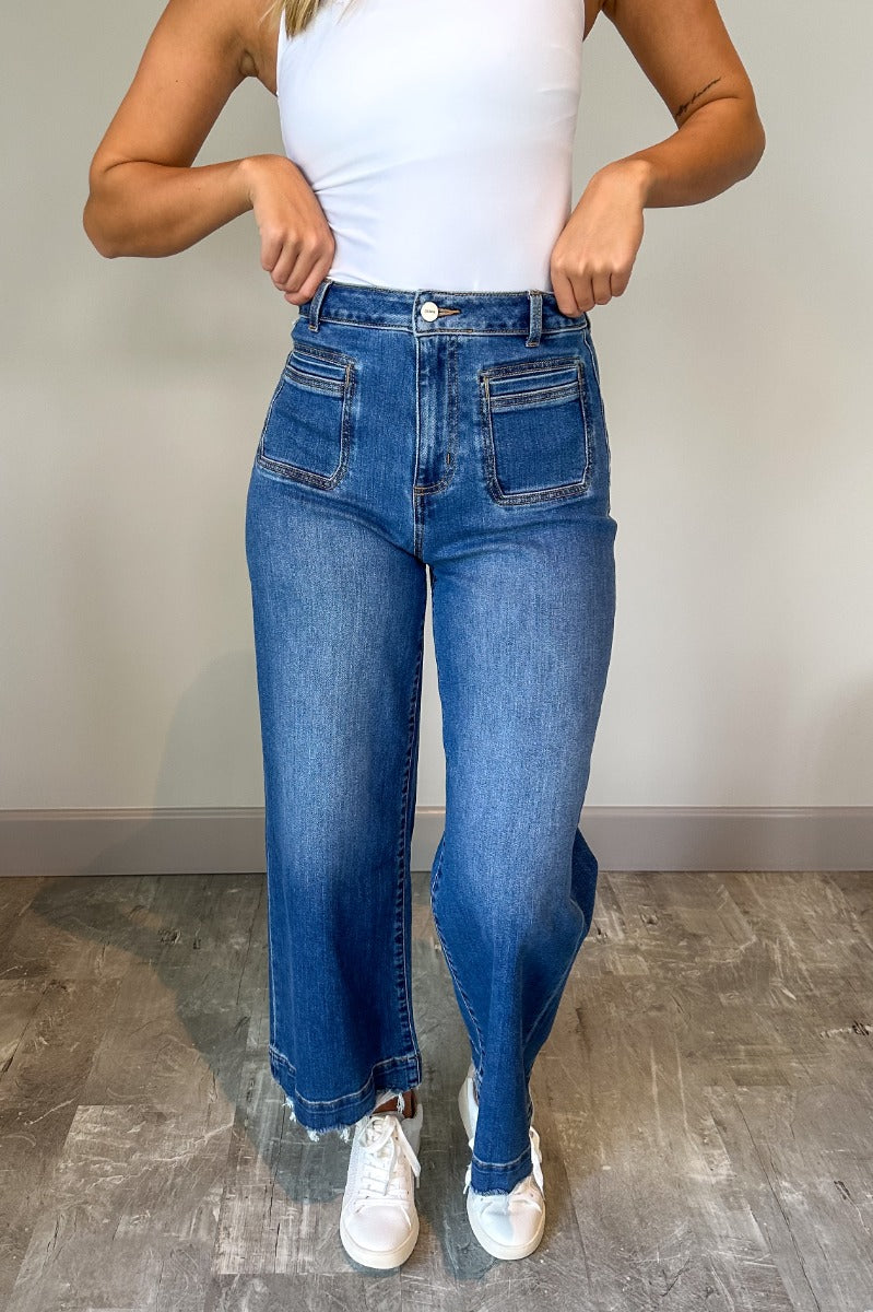 Front view of model wearing the Ceros: Florence Medium Wash Wide Leg Jeans which features medium blue denim fabric, a front zipper with a button closure, belt loops, a super high-rise waist, two front pockets, two back pockets, and wide cropped legs with 