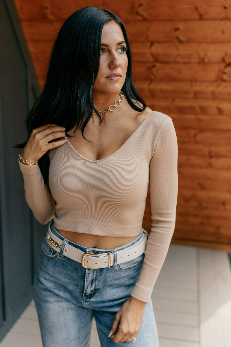 Front view of model wearing the Amara Nude Ribbed Long Sleeve Top which features nude ribbed fabric, cropped waist, v-neckline and long sleeves.