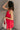 Side view of model wearing the Avery Red Bow Mini Dress which features crimson red sheen fabric, red lining, mini length, two front pockets, sweetheart neckline, adjustable straps, sleeveless, monochromatic side zipper with hook closure, smocked back and 