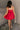 Back view of model wearing the Avery Red Bow Mini Dress which features crimson red sheen fabric, red lining, mini length, two front pockets, sweetheart neckline, adjustable straps, sleeveless, monochromatic side zipper with hook closure, smocked back and 