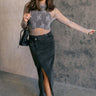 Full body front view of model wearing the Harlow Black Denim Front Slit Midi Skirt that has washed black denim fabric, a raw hem, midi length, a front slit, a slanted front zipper, pockets, and belt loops.