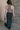 Back view of model wearing the Harlow Black Denim Front Slit Midi Skirt that has washed black denim fabric, a raw hem, midi length, a front slit, a slanted front zipper, pockets, and belt loops.