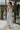 Full body back view of model wearing the Bexley Blue Denim Sleeveless Midi Dress that has light denim wash fabric, midi length, a monochrome stitch pattern, a v-neckline, and spaghetti straps.