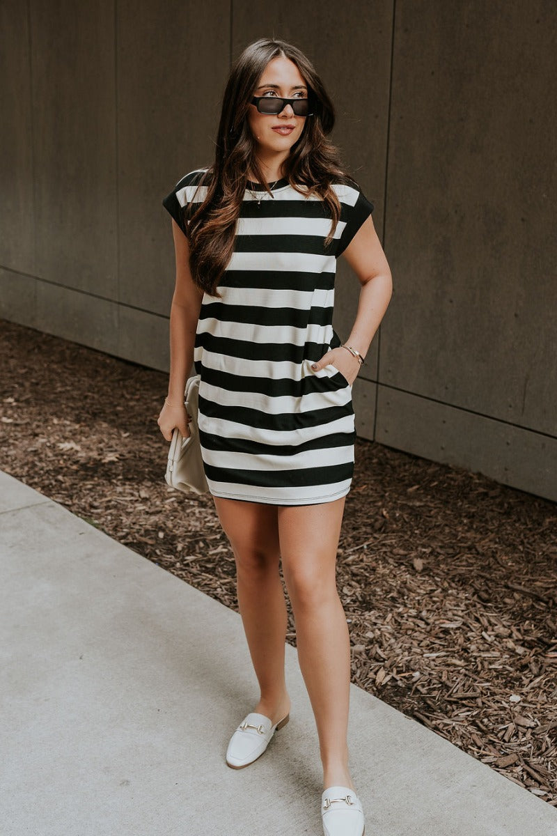 Full body view of model wearing the Esme Black & Cream Striped Dress which features black and cream ribbed fabric, striped pattern, mini length, two side pockets, round neckline and short sleeves.